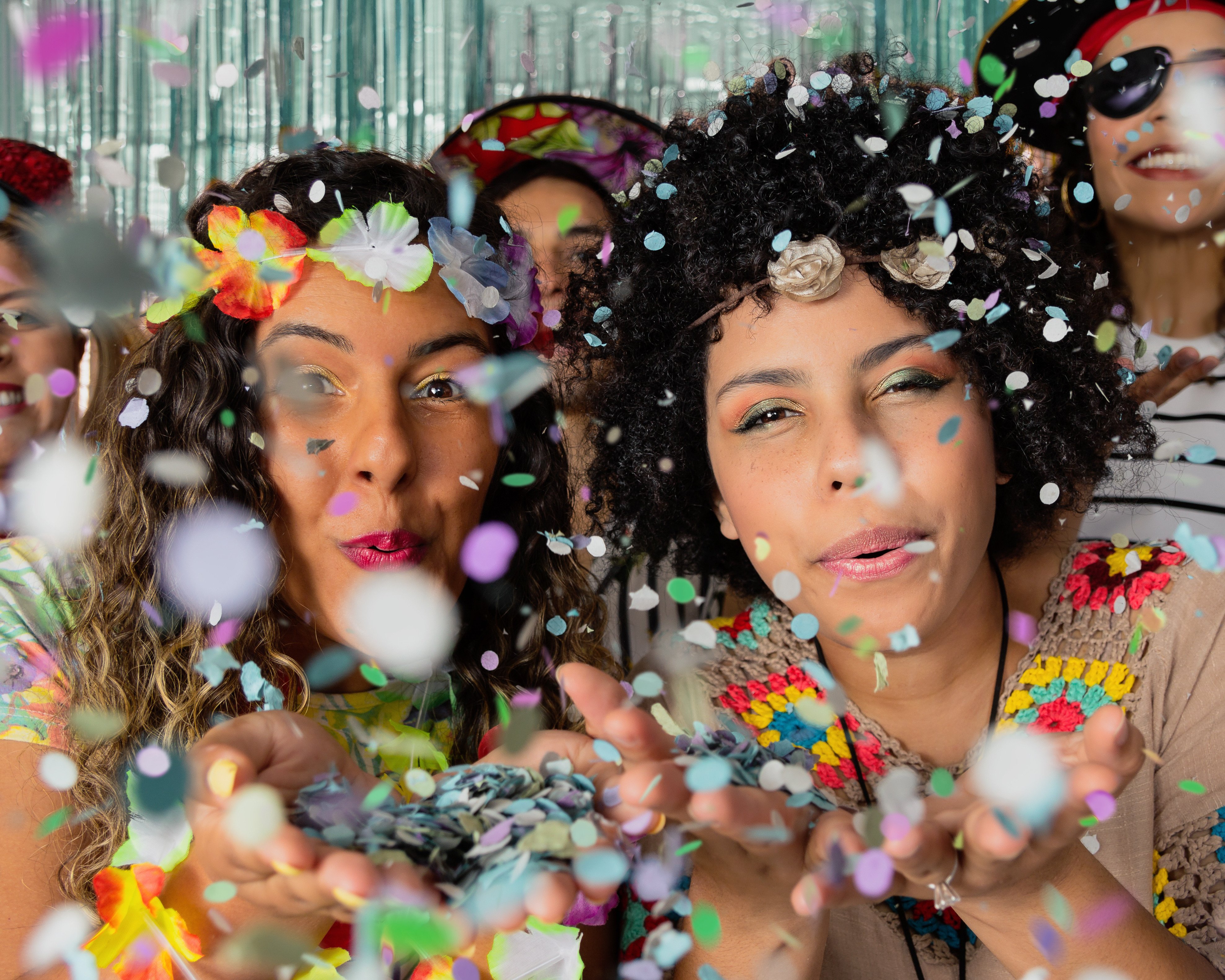 Two ladies blow confetti in the direction of the camera.